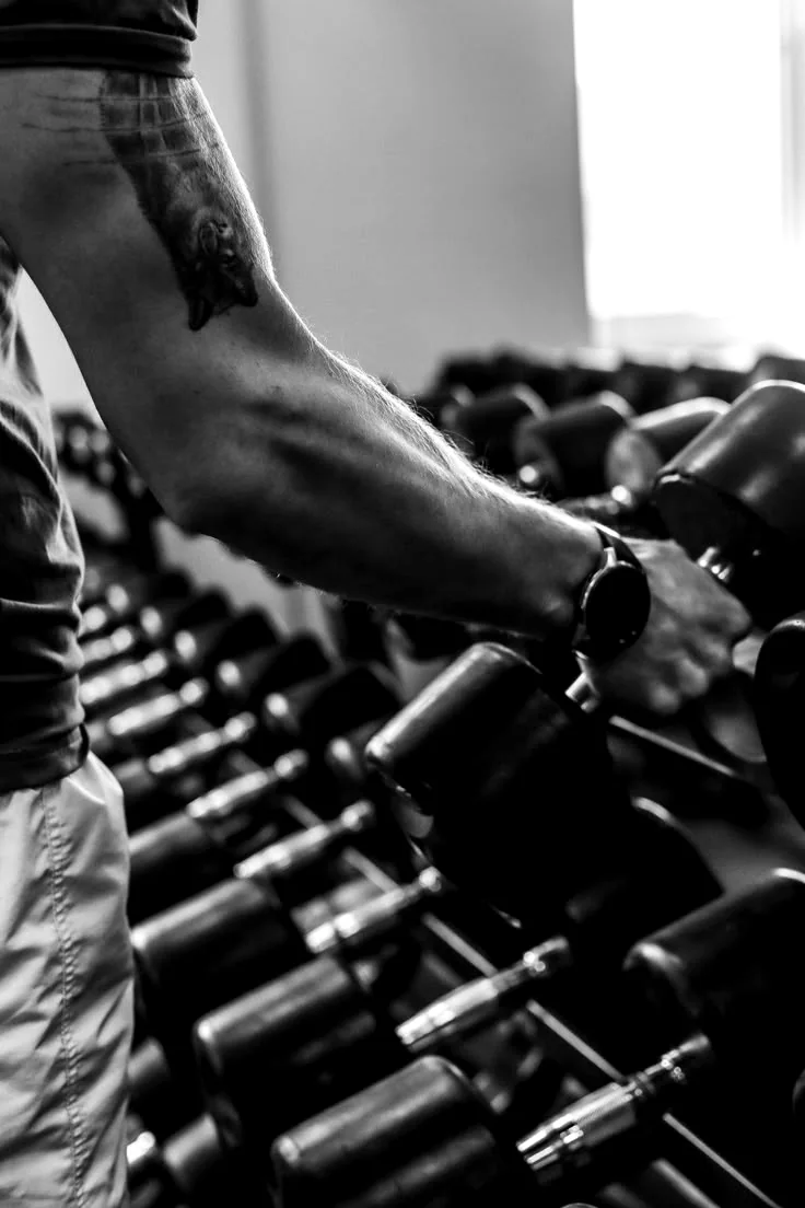 Atleta escolhendo halteres em um rack de academia, em preto e branco.