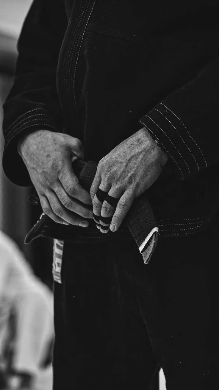 Praticante de Jiu-Jitsu ajustando a faixa-preta, em preto e branco.
