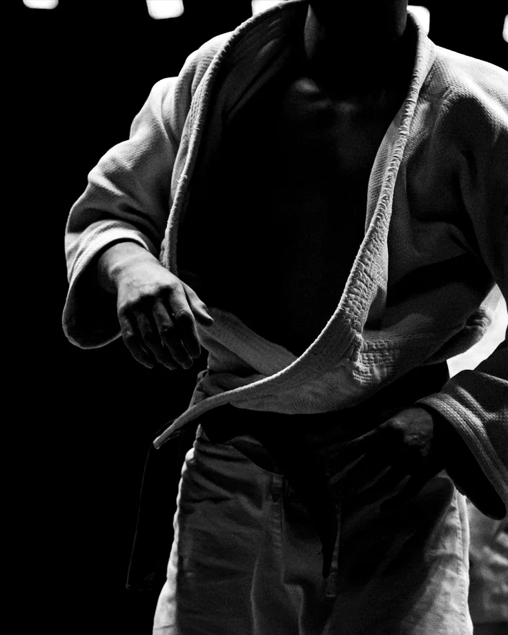 Atleta de judogi ajustando a faixa-preta antes do treino no tatame.